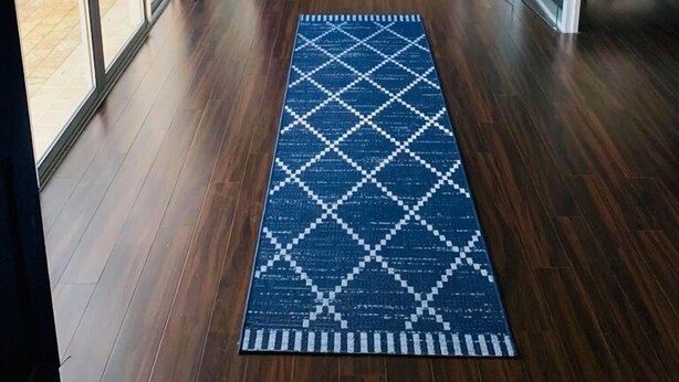 Un interior moderno con un largo pasillo, suelo de madera y una alfombra azul estampada.