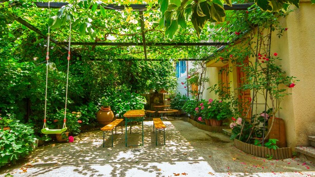 A sunlit garden with a pergola, wooden benches, and potted plants. - Kyveli Cottage (Foini)
