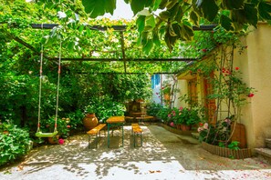 A sunlit garden with a pergola, wooden benches, and potted plants. - Kyveli Cottage (Foini)