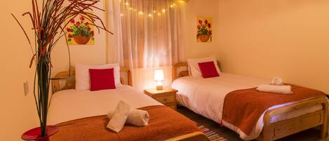 A hotel room with two beds, a wooden ceiling, a window with curtains, and a potted plant.