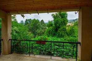 A covered balcony with a metal railing, overlooking a lush garden with various plants and flowers. - Kyveli Cottage (Foini)