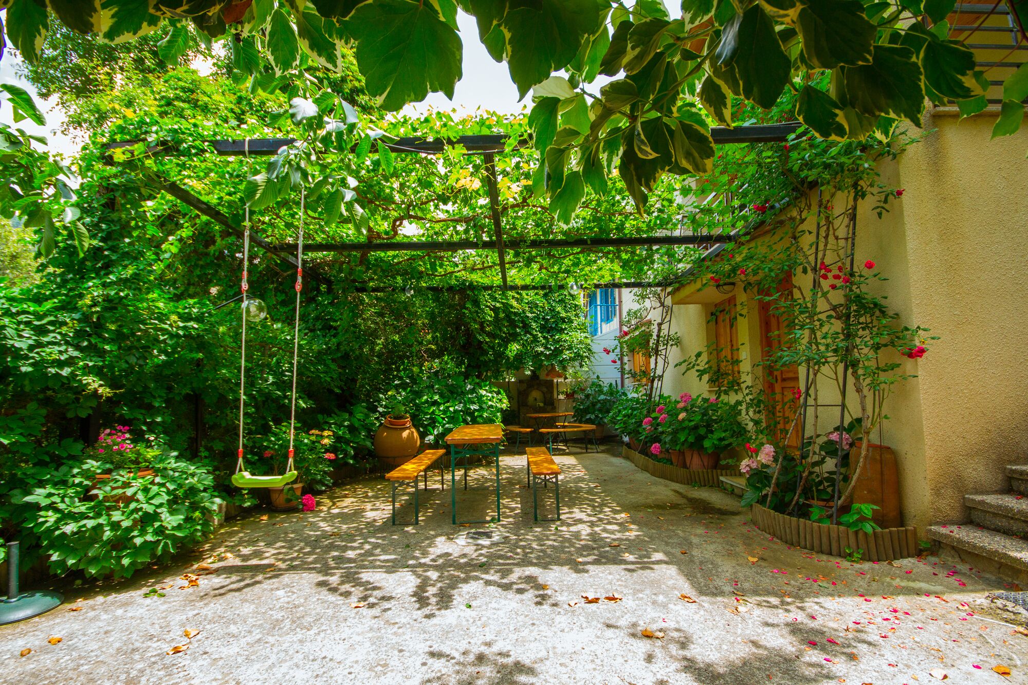 A garden patio with a swing, wooden tables, and a stone wall.