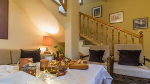 A cozy living room with a sofa set, a dining table with a centerpiece, and a staircase. - Kyveli Cottage (Foini)