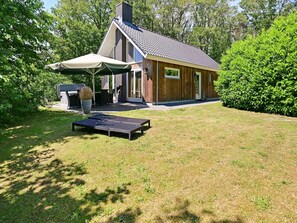 Ett modernt hus med en uteplats, en möblerad, överbyggd sittplats och en gräsmatta.