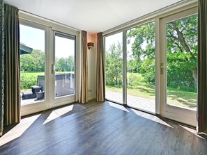 A room with large sliding glass doors leading to a garden, a wooden floor, and a small outdoor seating area. - Chalet in Reutum With Sauna and Nature (Reutum)