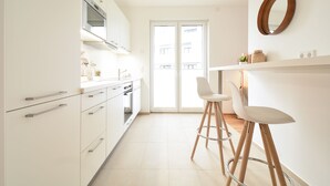 A modern kitchen with white cabinets, a stainless steel oven, and a large sliding glass door leading to a balcony. - Lunas Appartements in Essen (Essen)