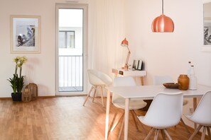 A dining area with a white table, white chairs, a copper pendant light, and a door leading outside. - Lunas Appartements in Essen (Essen)