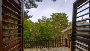 Un balcón con suelo de piedra, baranda de madera y vista a un edificio de piedra y árboles.