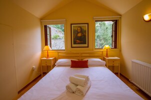 Una habitación de hotel con una cama grande, dos mesitas de noche con lámparas, un almohadón rojo y un cuadro de la Mona Lisa en la pared.
