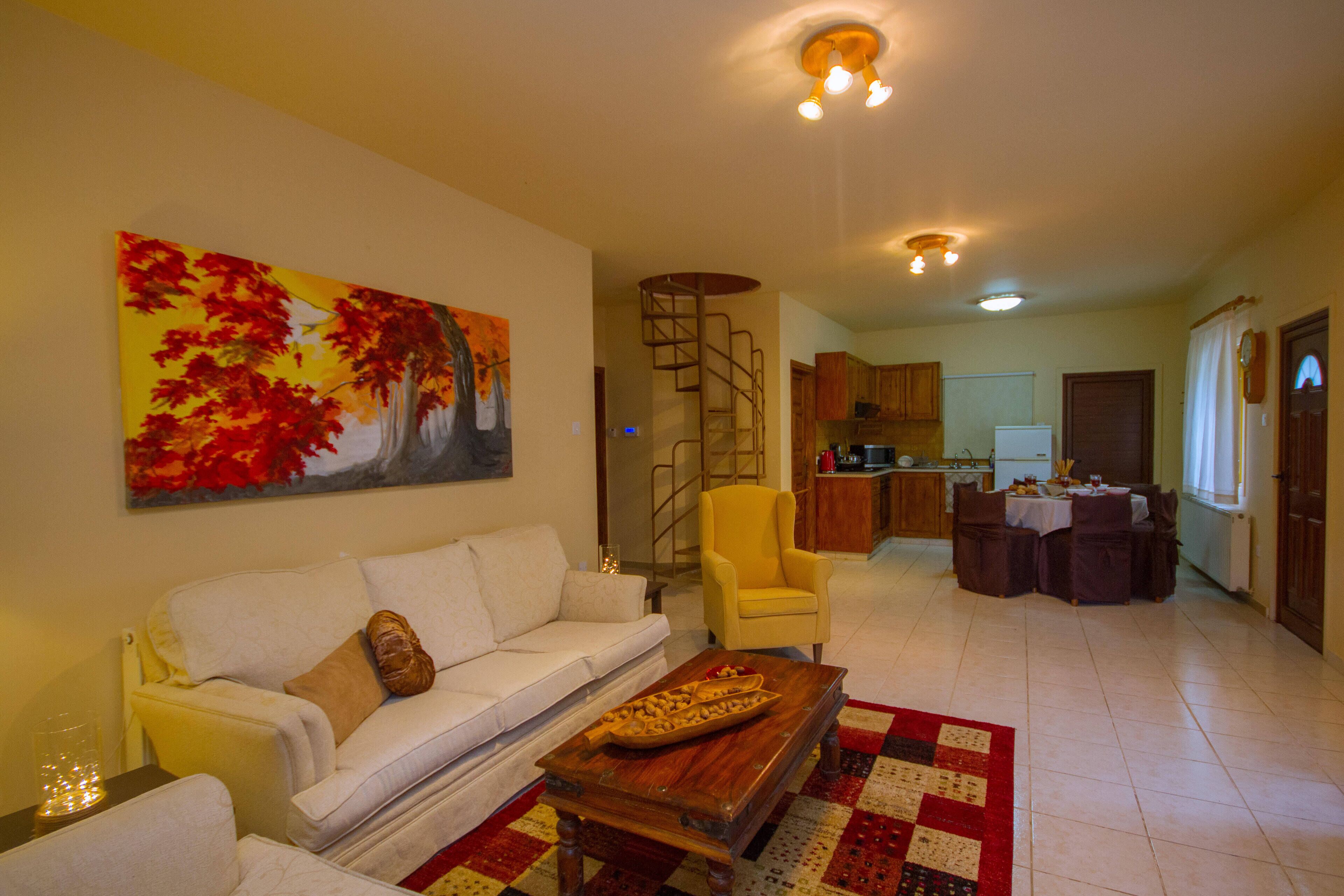 A living room with a sofa, armchair, coffee table, and a painting on the wall. There is a staircase leading to an upper level.