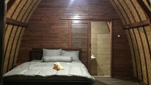 Un dormitorio en el ático con techo de madera, una cama con almohadas y una mesita de noche.