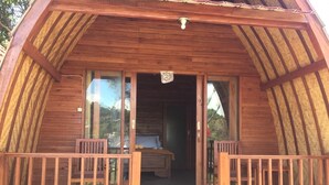 Una cabaña de madera con porche, una cama y un ventanal pequeño.