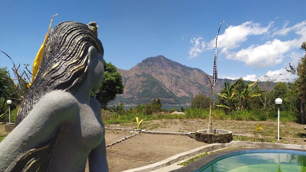 Una estatua de mujer junto a una piscina, con una montaña al fondo.