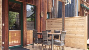 An outdoor wooden deck with a table and chairs, a wooden fence, and a door leading to a covered area. - Snug Holiday Home in Sankt Georgen ob Murau near Kreischberg (Sankt Georgen am Kreischberg)