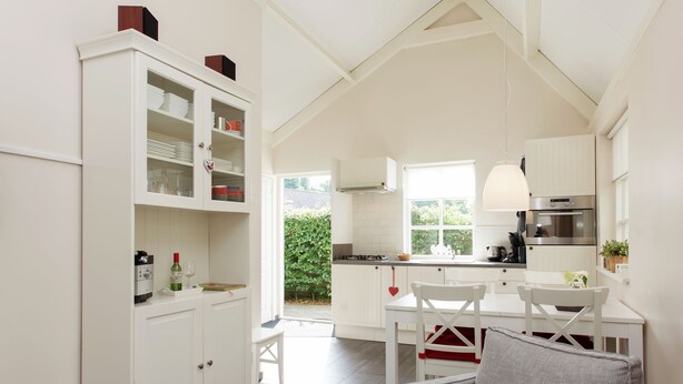 A modern kitchen with white cabinetry, a dining area with a white table and chairs, and a view of a garden through a window. - Holiday Home in Ravenstein With Garden (Overlangel)