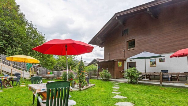 A well-maintained outdoor patio area with a wooden building, stone pathway, and outdoor seating with umbrellas. - Spacious Apartment in Saalbach-hinterglemm near Ski Area (Saalbach-Hinterglemm)