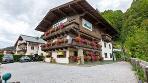 A traditional wooden building with balconies adorned with colorful flowers, a sign indicating it is a pension, and a gravel driveway. - Spacious Apartment in Saalbach-hinterglemm near Ski Area (Saalbach-Hinterglemm)