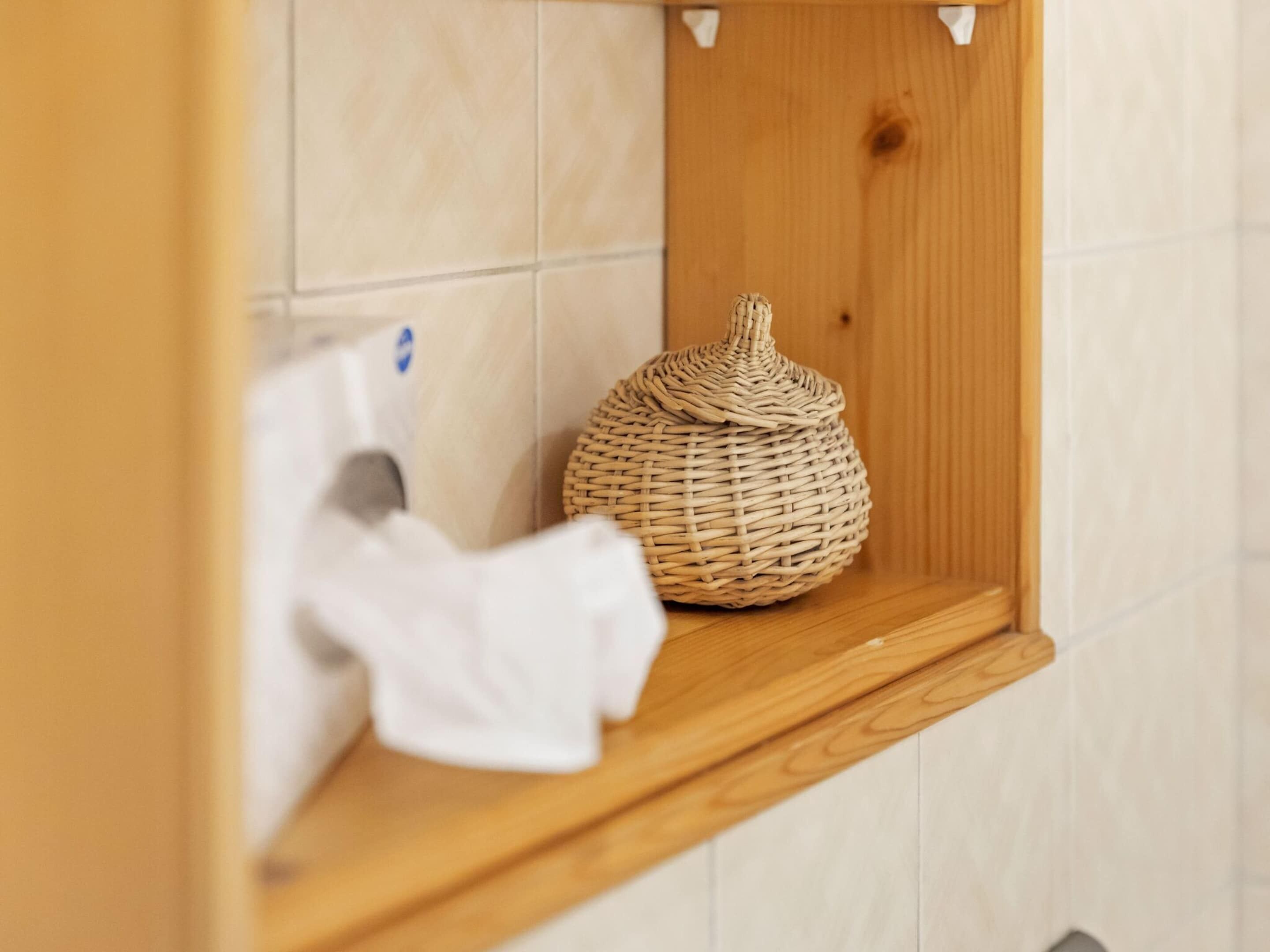 Een badkamer met een houten plankje met een geweven mand en een witte handdoek.