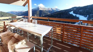 A wooden deck with a table and chairs, overlooking a mountainous landscape with a lake.