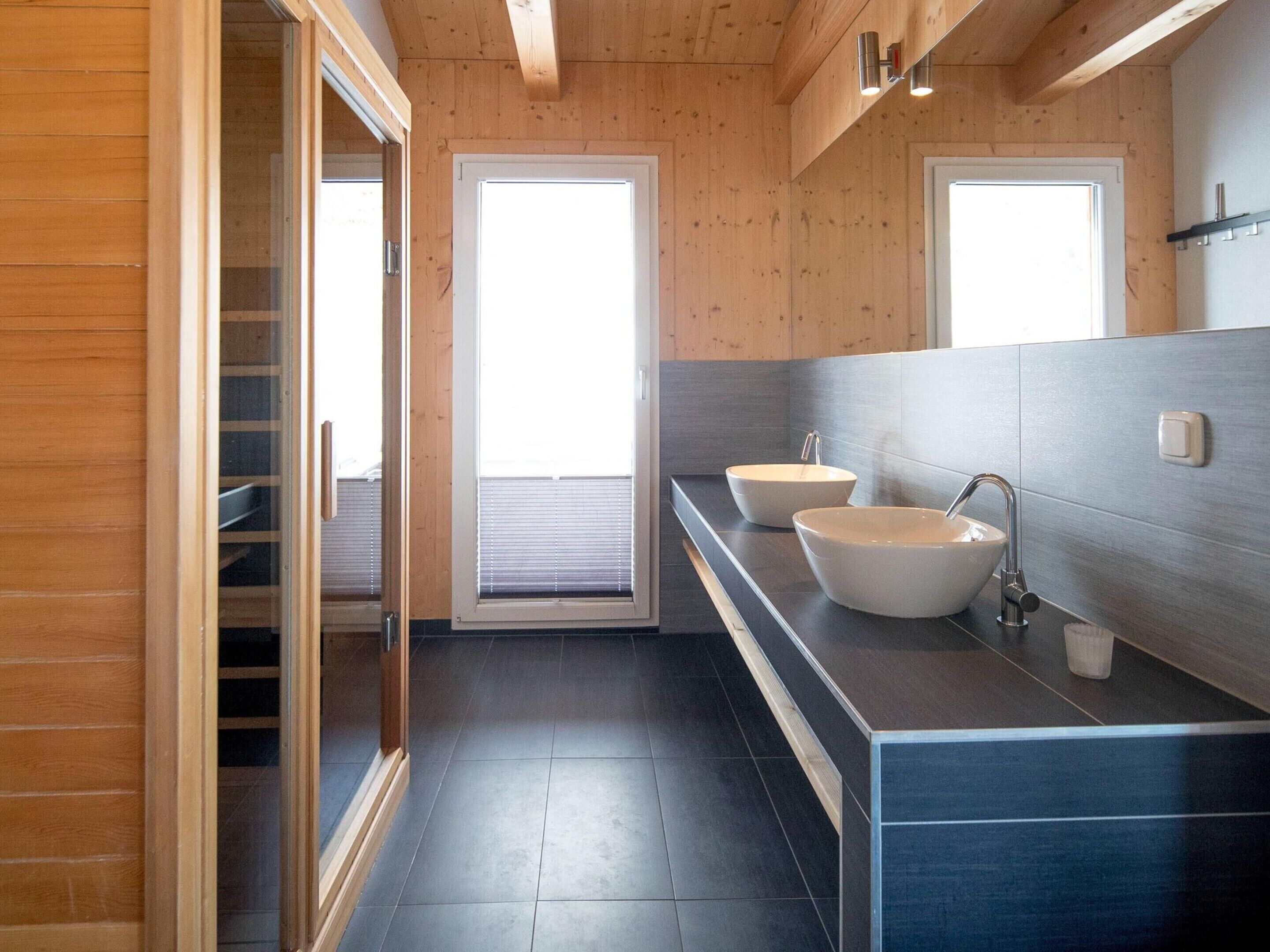 Ein modernes Badezimmer mit Holzwänden, zwei Waschbecken und einem großen Fenster.