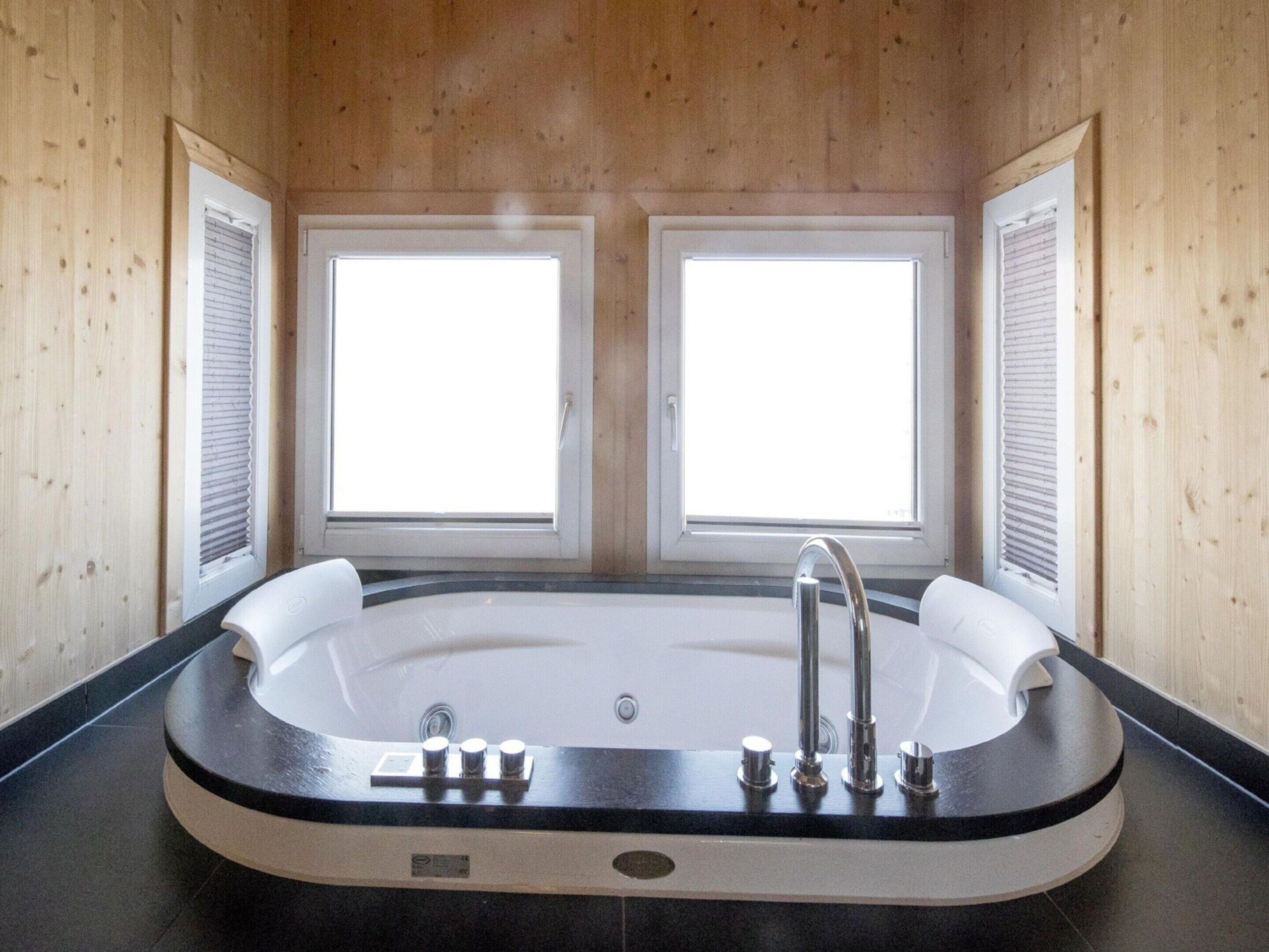 A modern bathroom with a freestanding bathtub, two windows, and wooden walls.