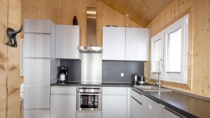 A modern kitchen with white cabinets, stainless steel appliances, and a wooden ceiling.