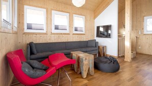 A modern interior with a wooden ceiling, a grey sofa, red chairs, a wooden coffee table, and a black bean bag.
