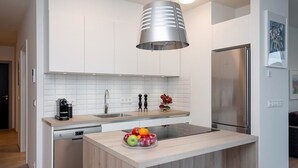 Et moderne køkken med hvide skabe, et rustfrit stål køleskab, en opvaskemaskine og en skål med frugt på øen.