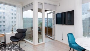 En moderne stue med en skydedør til en balkon, et fladskærms-tv på væggen og et spiseområde med et rundt bord og stole.