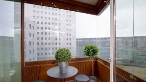 En balkon med et bord, to stole, en potteplante og udsigt til en høj bygning.