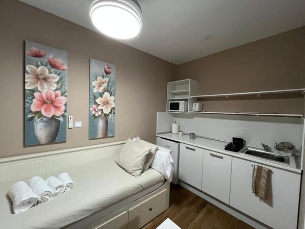 Una habitación compacta con cama, kitchenette y dos cuadros de flores colgados en la pared.