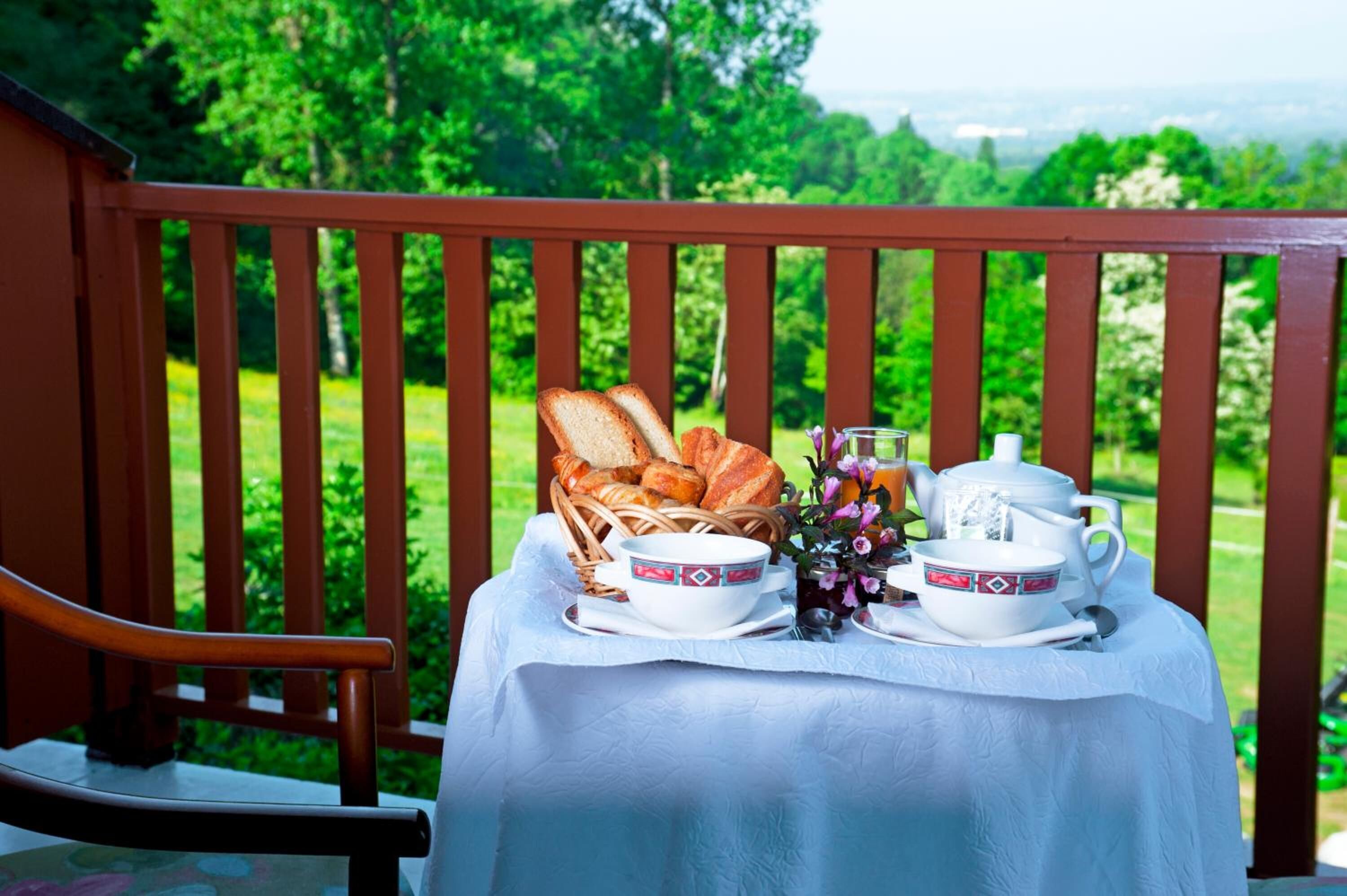 Ein Tisch gedeckt mit Brot, einer Schüssel, einem Teekännchen und Tassen auf einem Balkon mit Blick ins Grüne.