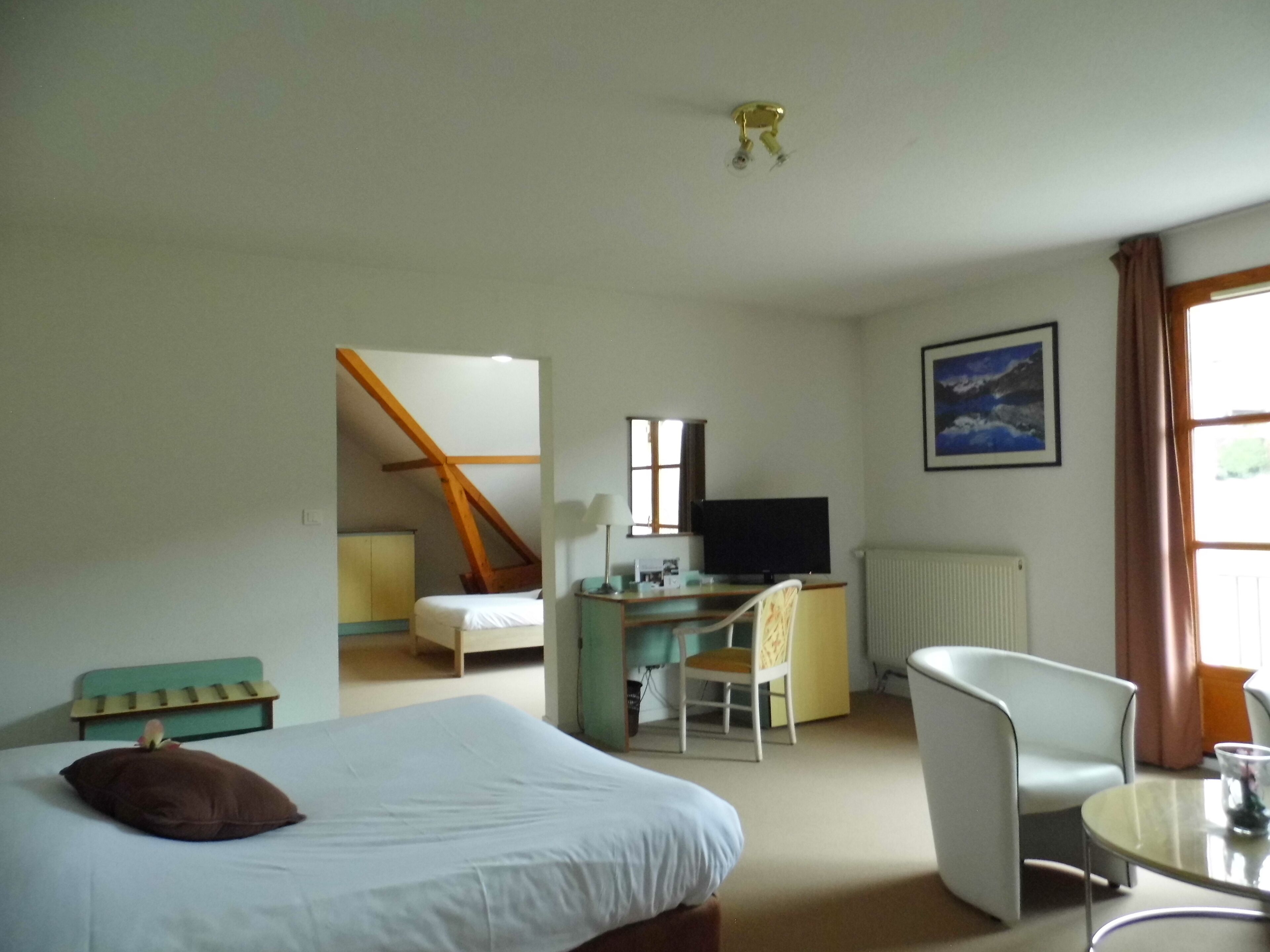 Una habitación de hotel con una cama, un escritorio con computadora, una silla, un televisor y una ventana con cortinas.