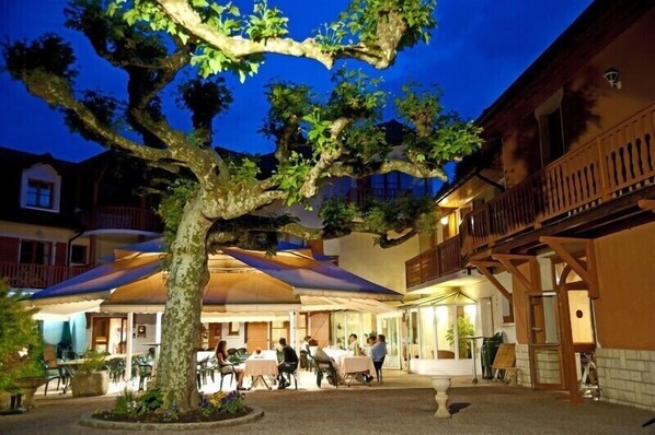 A courtyard with outdoor seating, a large tree, and a building with a balcony.