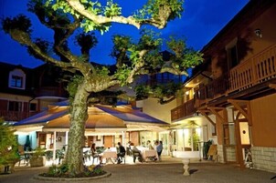 Une cour avec des sièges en plein air, un grand arbre et un bâtiment doté d’un balcon.