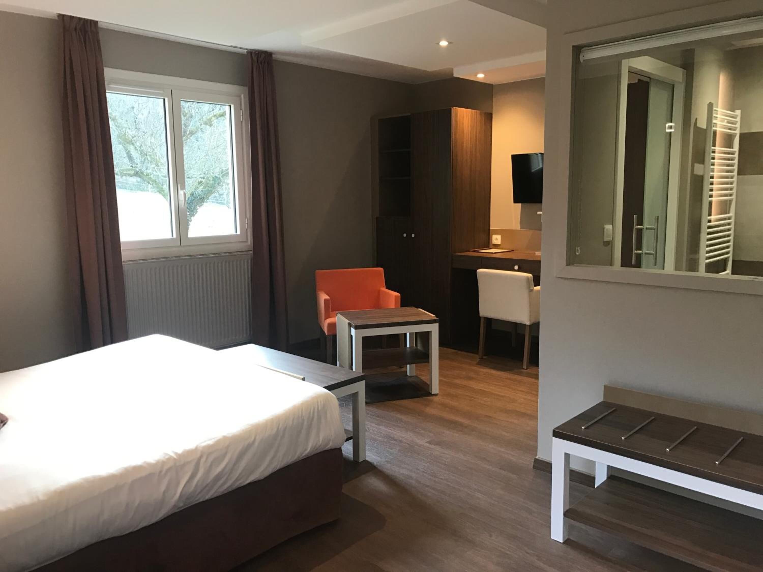 A modern hotel room with a bed, a desk, an orange chair, and a bench.