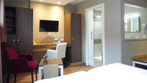 A hotel room with a bed, a desk with a chair, a TV mounted on the wall, and a shower area. - Hotel Restaurant Les Bergeronnettes (Champagneux)