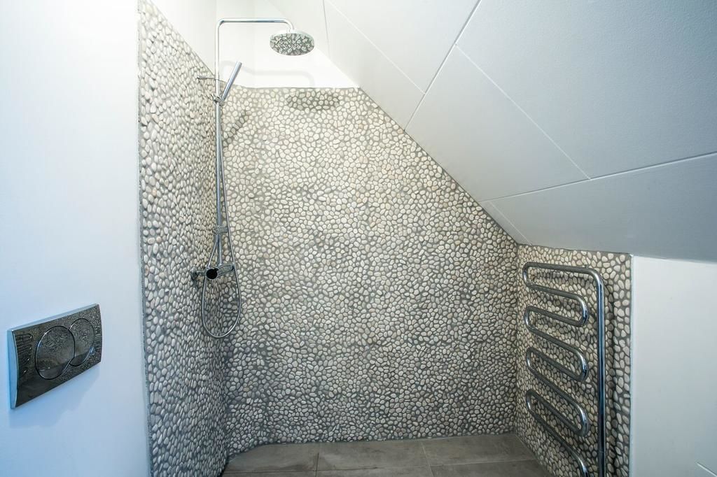 A shower with a pebble-textured wall, a metal handrail, and a control panel.