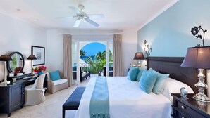 Habitación de hotel con cama, escritorio, silla, ventilador de techo y vistas al exterior.
