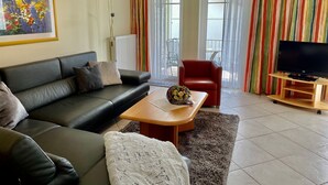 A living room with a black sofa, a red chair, a wooden coffee table with a bouquet, a TV on a wooden stand, and a colorful striped curtain. - Guesthouse wine paradise (Hochstadt (Pfalz))