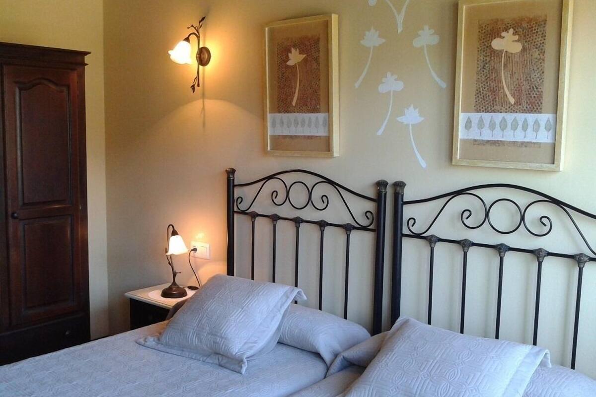 A bedroom with a bed, two bedside tables, a wall-mounted lamp, and framed artwork.