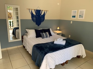 A bedroom with a bed, a hanging macrame wall decoration, a bedside lamp, and two framed pictures on the wall. - Pousada Magias de Paraty (Paraty)
