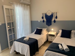 A hotel room with two beds, a nightstand, a wall-mounted macrame decoration, and a sliding glass door. - Pousada Magias de Paraty (Paraty)