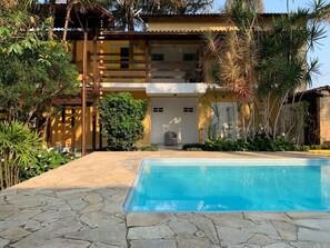 A swimming pool with stone tiles, surrounded by lush greenery and a two-story building with a balcony. - Pousada Magias de Paraty (Paraty)