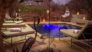 A poolside area with lounge chairs, a hanging chair, and a small pool with a blue light. - Ukuthula Bush Lodge (Hoedspruit)