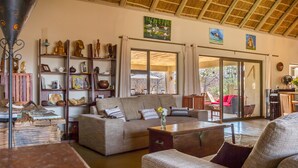 A spacious living area with a sofa, coffee table, and shelves with various decorative items. - Ukuthula Bush Lodge (Hoedspruit)