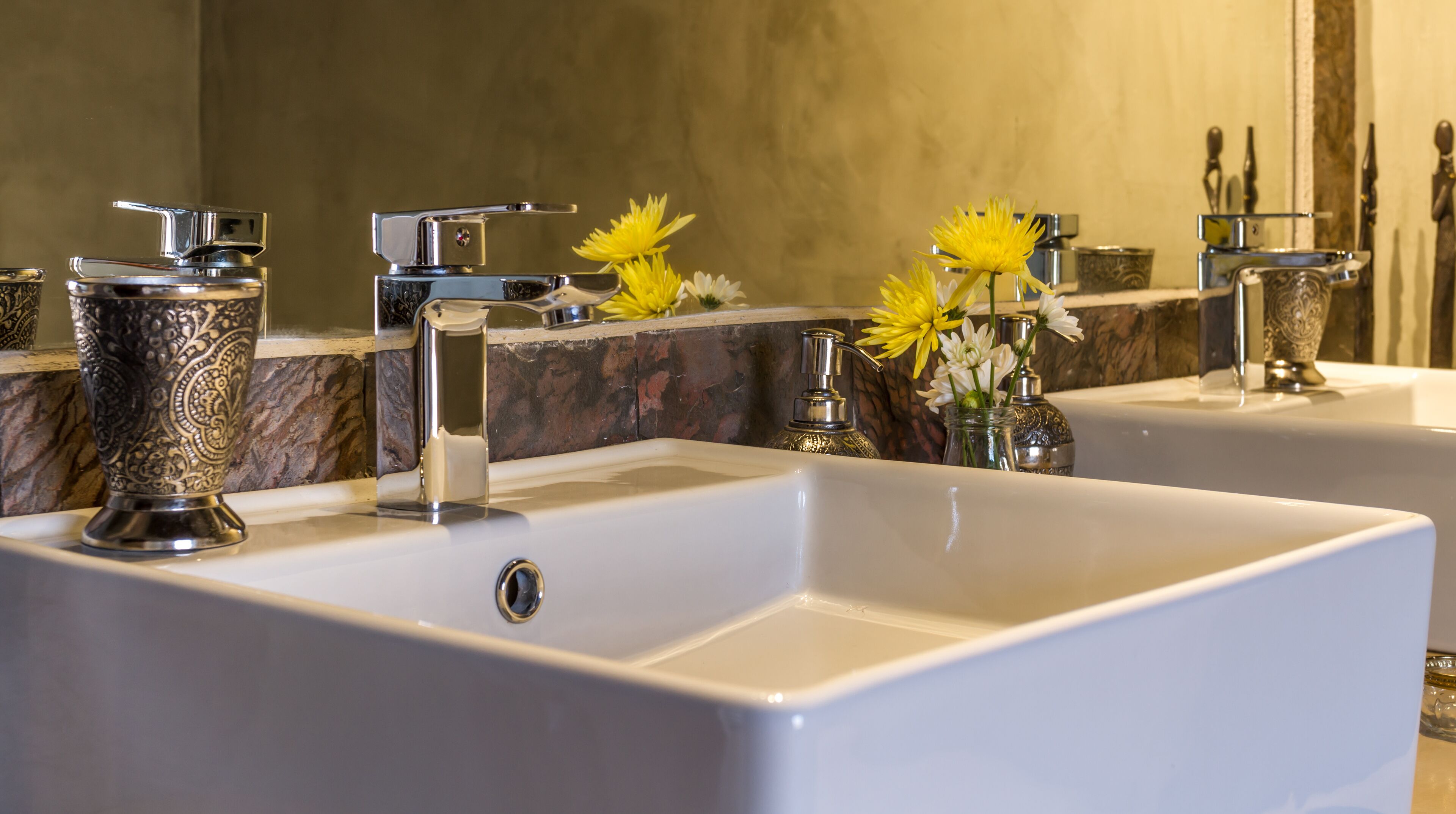 Un bagno con due lavabi, uno specchio e vasi decorativi con fiori.