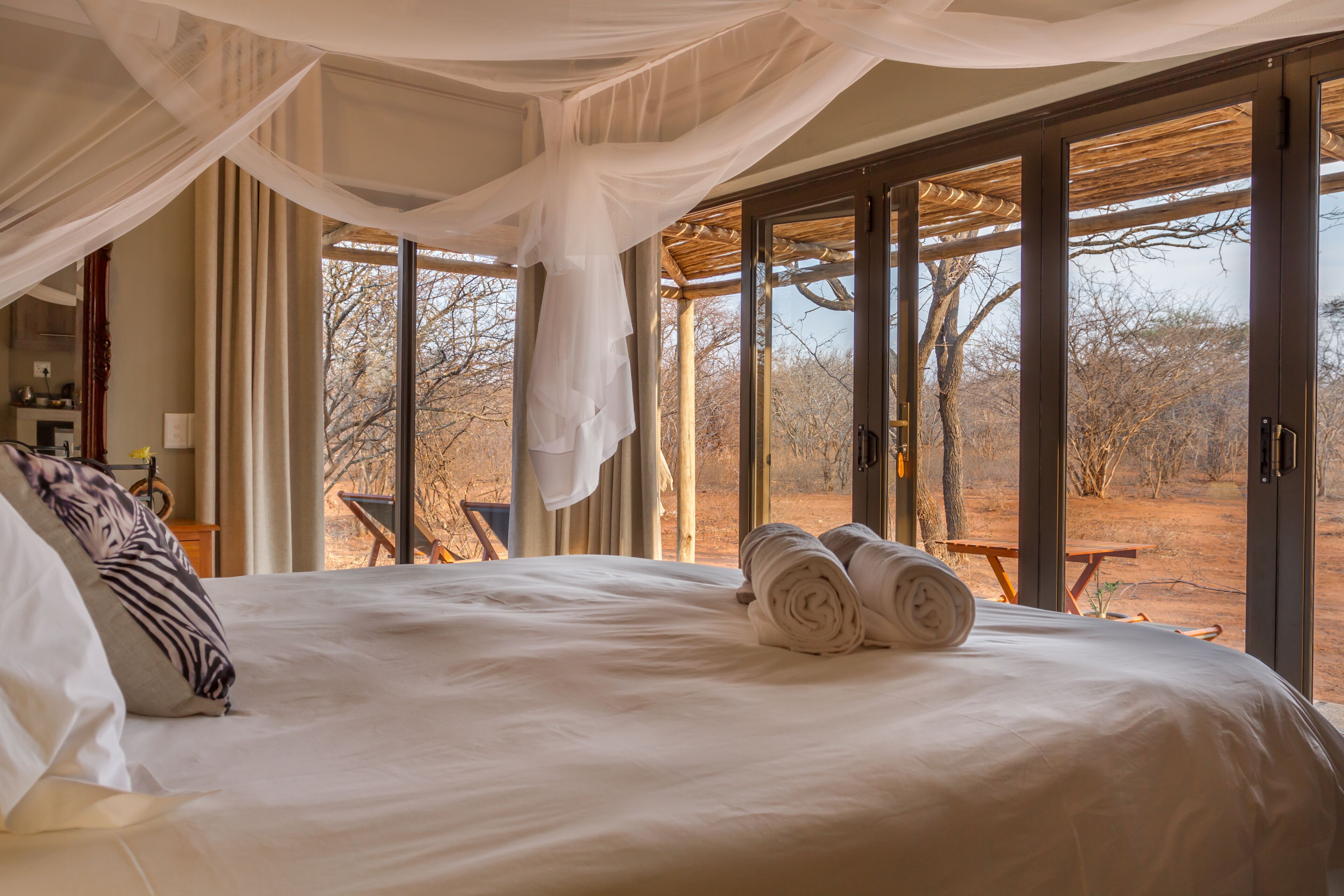 Una cama grande con ropa blanca, un dosel y vistas al exterior a través de amplios ventanales.