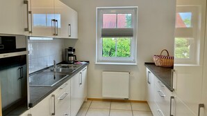 Ett modernt kök med vita skåp, en svart bänkskiva, en inbyggd ugn och ett fönster med utsikt över grönområden.