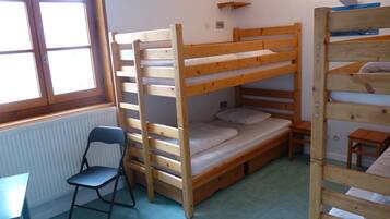 Een slaapkamer met een stapelbed, een klein tafeltje en stoel, een radiator en een raam.